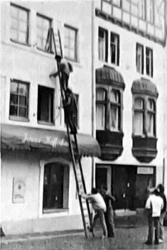 Zwei Männer auf einer Leiter an einer Hausfassade, zwei weitere halten die Leiter