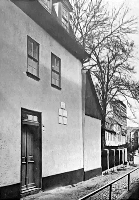 Weiß verputztes Haus mit Holztür und vier kleinen Tafeln neben dem Eingang